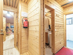 A wooden interior with a fire extinguisher mounted on the wall, a door leading to a bathroom, and a visible tiled floor.