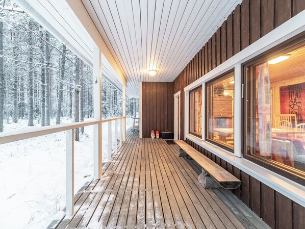 A wooden deck with benches, large windows, and a view of a snowy forest.