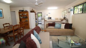 A living room with a sofa, a glass coffee table, and a dining area with a table and chairs. - Seaward Cottage, Nelly Bay (NELLY BAY)