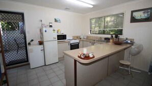 A compact kitchen with a refrigerator, microwave, stove, and a small dining area with a chair. - Seaward Cottage, Nelly Bay (NELLY BAY)