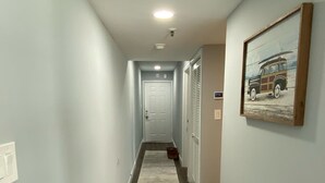 A hallway with a grey carpet, a door at the end, and a framed picture on the wall. - Wake up to the sunrise over the Atlantic! Beautiful ocean views from balcony  (North Myrtle Beach)