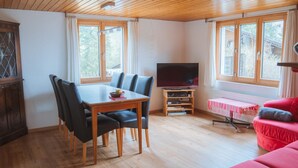 A cozy living room with a wooden ceiling, a dining area with a table and chairs, a television on a wooden stand, and a red sofa. - Burkhalter by Interhome (Zweisimmen)