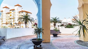 A courtyard with a view of a hotel building, potted plants, and a bench. - Reina Sofia II by Interhome (Estepona)