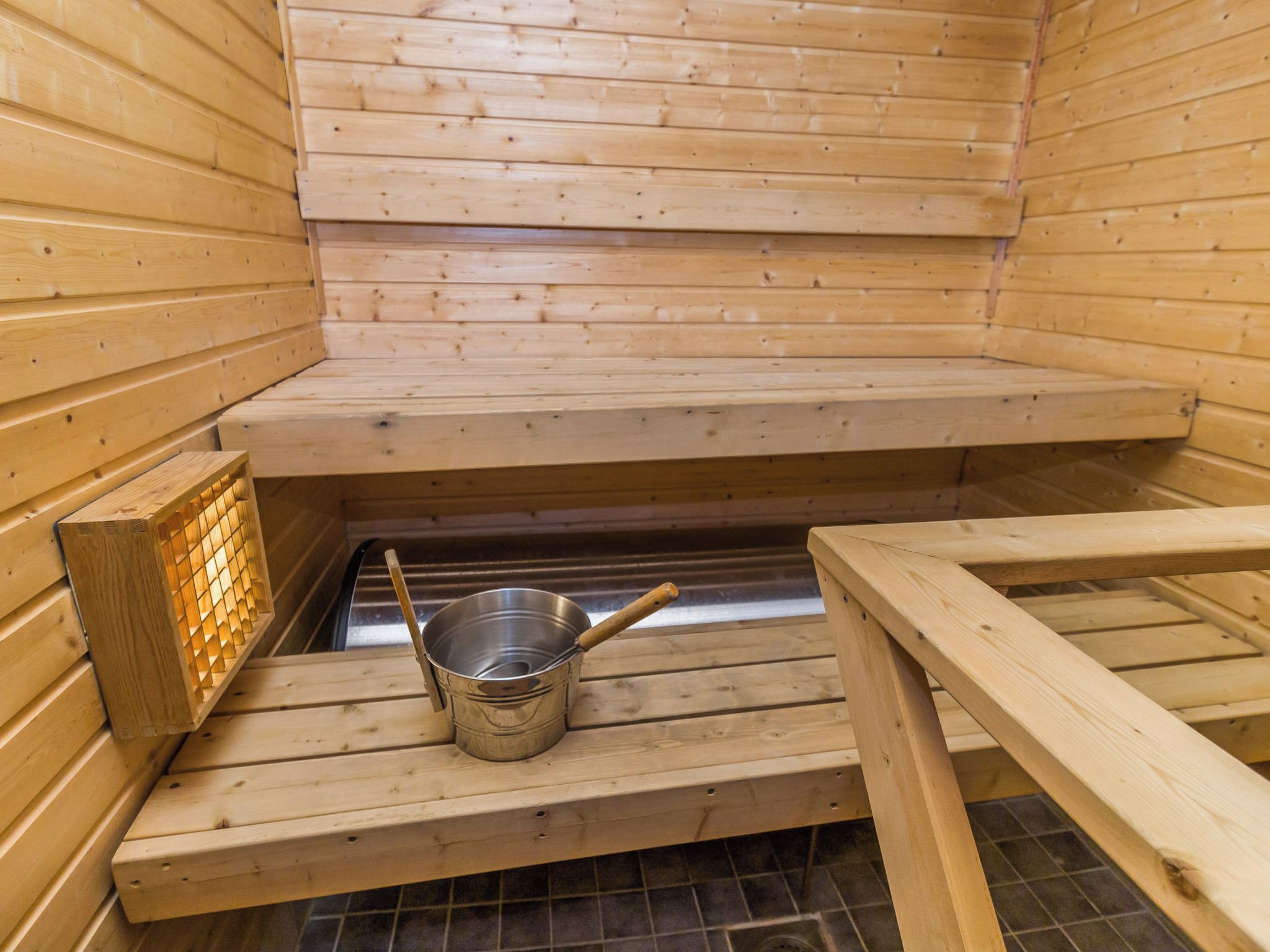 Un sauna avec des bancs en bois et un seau en métal.
