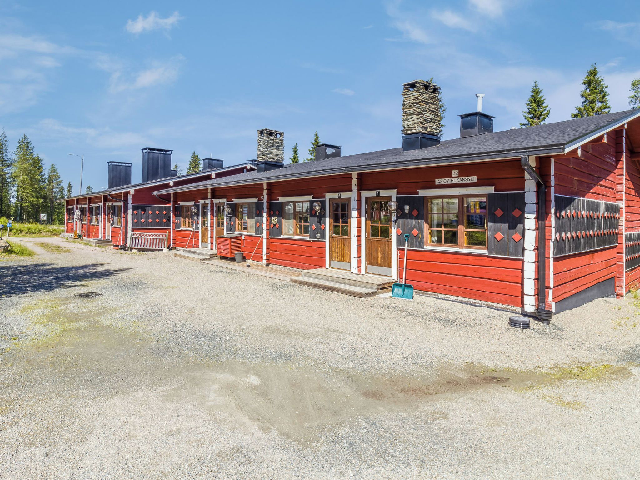 A row of red wooden cabins with numbered doors, a gravel driveway, and a clear sky.