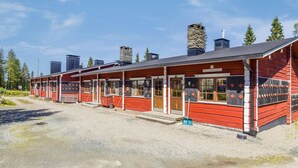 Une rangée de cabanes en bois rouges, dotées d’un porche couvert, numérotées de 1 à 22, et une enseigne indiquant « AS OY RUKANSYLI ».