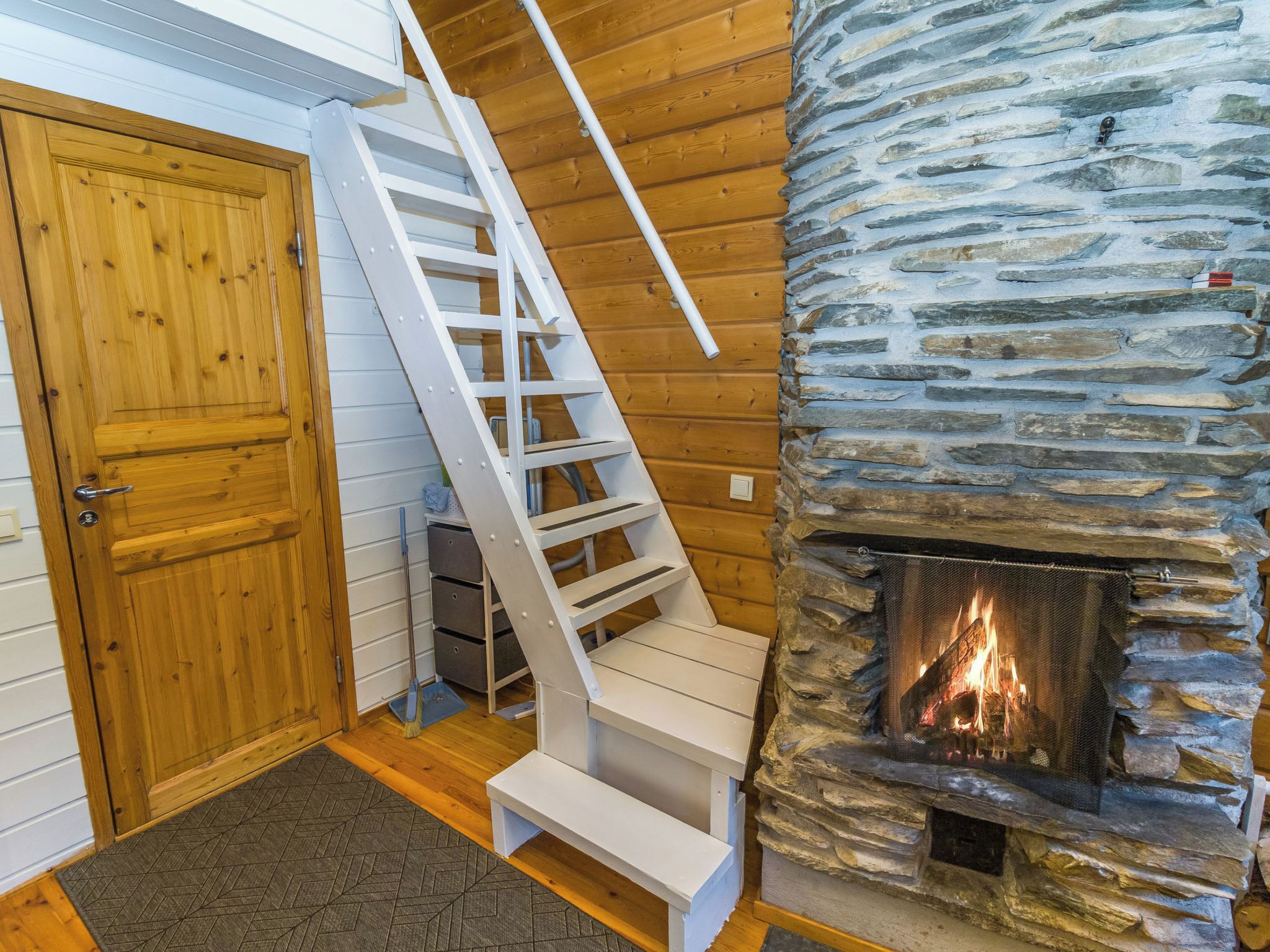 A wooden staircase leading to a stone fireplace with a fire.