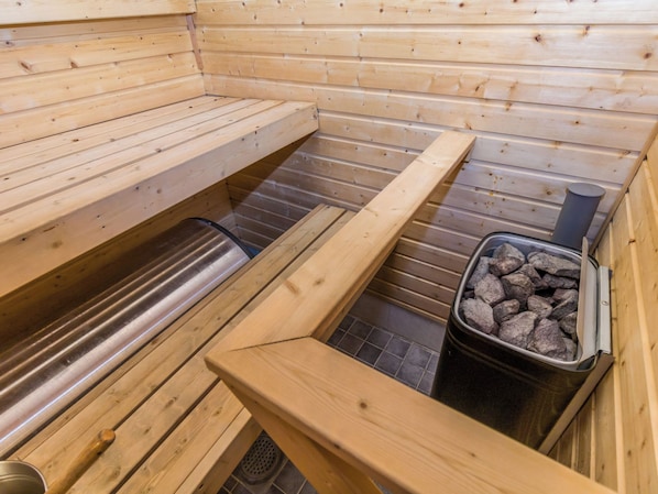 Una sauna con bancos de madera, un banco de metal y un recipiente con piedras para calentar.
