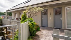 Ein eingeschossiges Gebäude mit überdachter Veranda, Holzzaun und kleinem Garten mit Pflanzen und Blumen.