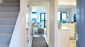 Eine moderne Küche mit einer zentralen Kochinsel, ein Essbereich mit einer Couch und Sesseln sowie eine Treppe zu einer weiteren Ebene.