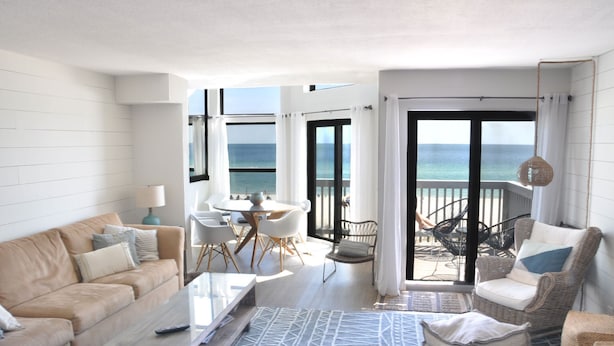Ein modernes Wohnzimmer mit Sofa, Couchtisch und Essbereich. Ein Balkon bietet Blick aufs Meer.