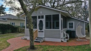 Ein kleines, eingeschossiges Haus mit Veranda, überdachter Eingangspforte und einer kleinen Sitzgelegenheit im Freien.