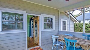 Eine überdachte Veranda mit Holztisch und blauen Stühlen, eine zur Innenseite führende Tür und ein Deckenventilator.