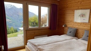A bedroom with a large window, wooden walls, a bed with two pillows, and a framed picture on the wall. - Brunnquell by Interhome (Bettmeralp)