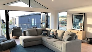A modern living room with a large sectional sofa, a glass door leading to an outdoor terrace, and a view of a blue building.
