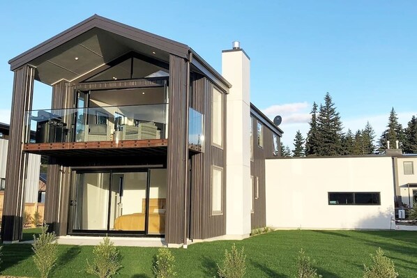 A modern two-story house with a balcony, large windows, and a well-maintained lawn.