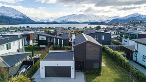 A residential area with modern houses, a lake, and snow-capped mountains in the background.