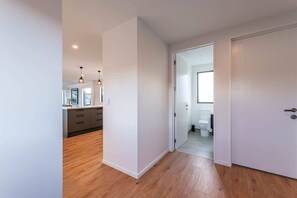 A hallway leading to a kitchen and bathroom with wooden flooring and white walls.