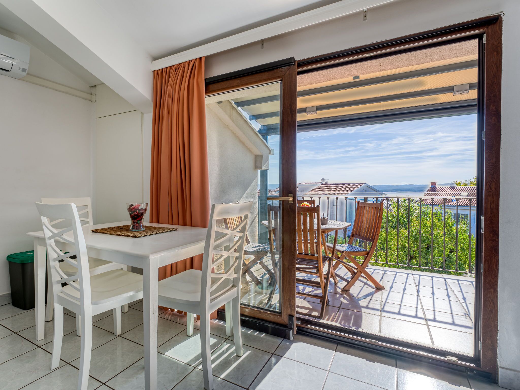 Ein Balkon mit Tisch und Stühlen, Blick auf Gebäude und Wasser, und eine grüne Umzäunung.