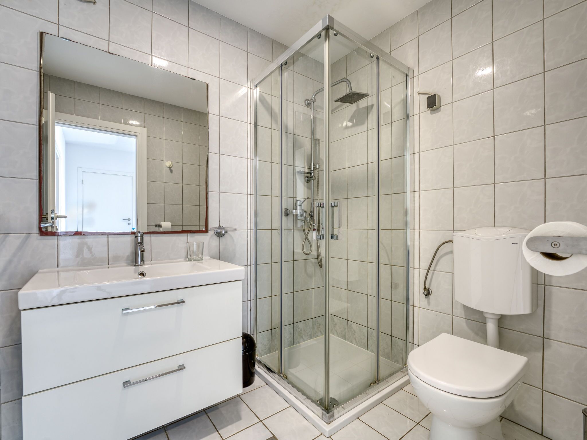 Uma casa de banho moderna com chuveiro envidraçado, lavatório branco com espelho e sanita.