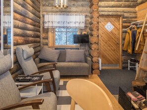 Ein gemütliches Blockhaus-Interieur mit einer Couch, Sesseln, einem Fernseher und einem Kleiderständer mit Jacken.