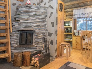 L’intérieur chaleureux d’un chalet avec une cheminée en pierre, des meubles en bois et une vue sur les arbres enneigés par la fenêtre.