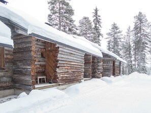 Eine Reihe von Blockhütten mit schneebedeckten Dächern, umgeben von hohen Kiefern.
