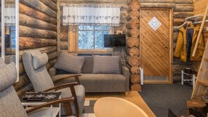 L’intérieur d’une cabane en rondins, avec un canapé, des fauteuils, un téléviseur et un porte-manteau.