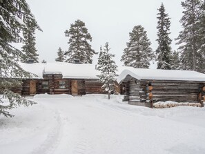 Une cabane en rondins, dont le toit est recouvert de neige et l’extérieur en bois, entourée d’arbres chargés de neige.