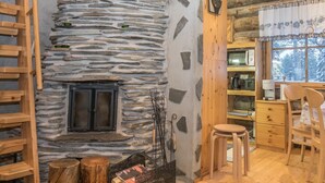 Un intérieur de chalet chaleureux avec une cheminée en pierre, des meubles en bois et une vue sur le paysage enneigé.