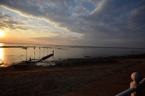 Una playa con un muelle que se adentra en aguas tranquilas, un cielo despejado y una puesta de sol.