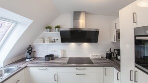 Et moderne køkken med lyse skabe, emhætte i rustfrit stål, indbygget ovn og et vindue med naturligt lys.