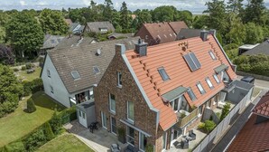 Et moderne hus med to etager, skråt tag, store vinduer og en terrasse med udendørs møbler.
