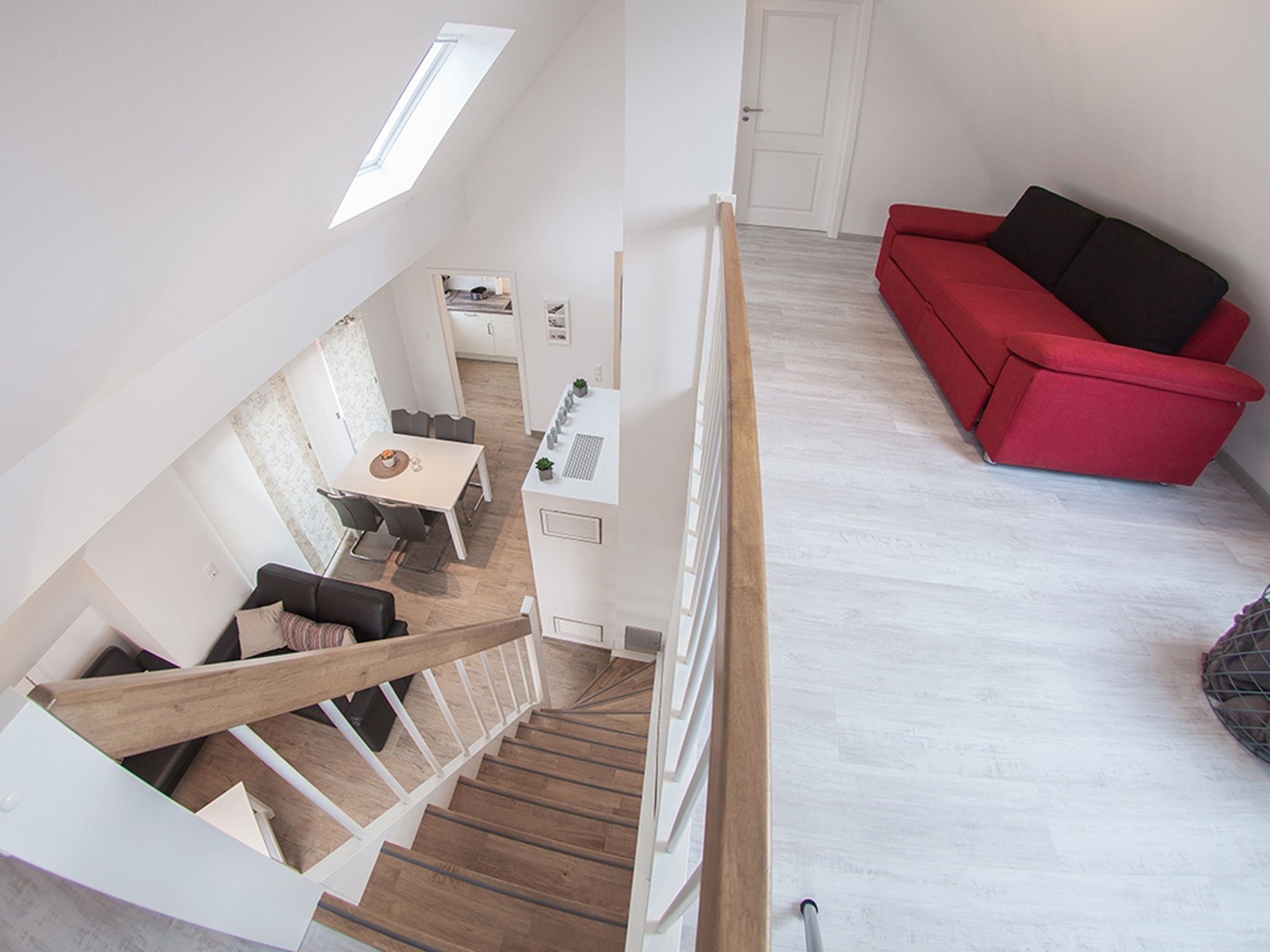 A modern interior with a staircase, a dining area, a red sofa, and a kitchen.