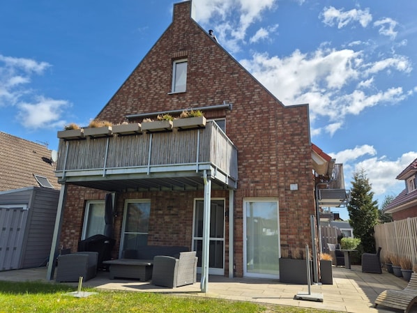 Une maison à deux étages dotée d’un balcon, d’une terrasse avec mobilier d’extérieur et d’une façade en briques.