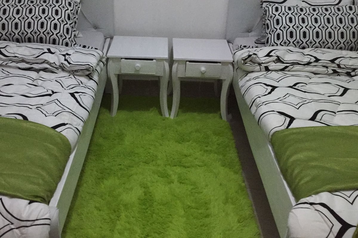 A twin bedroom with two beds, a small table, and a green carpet.