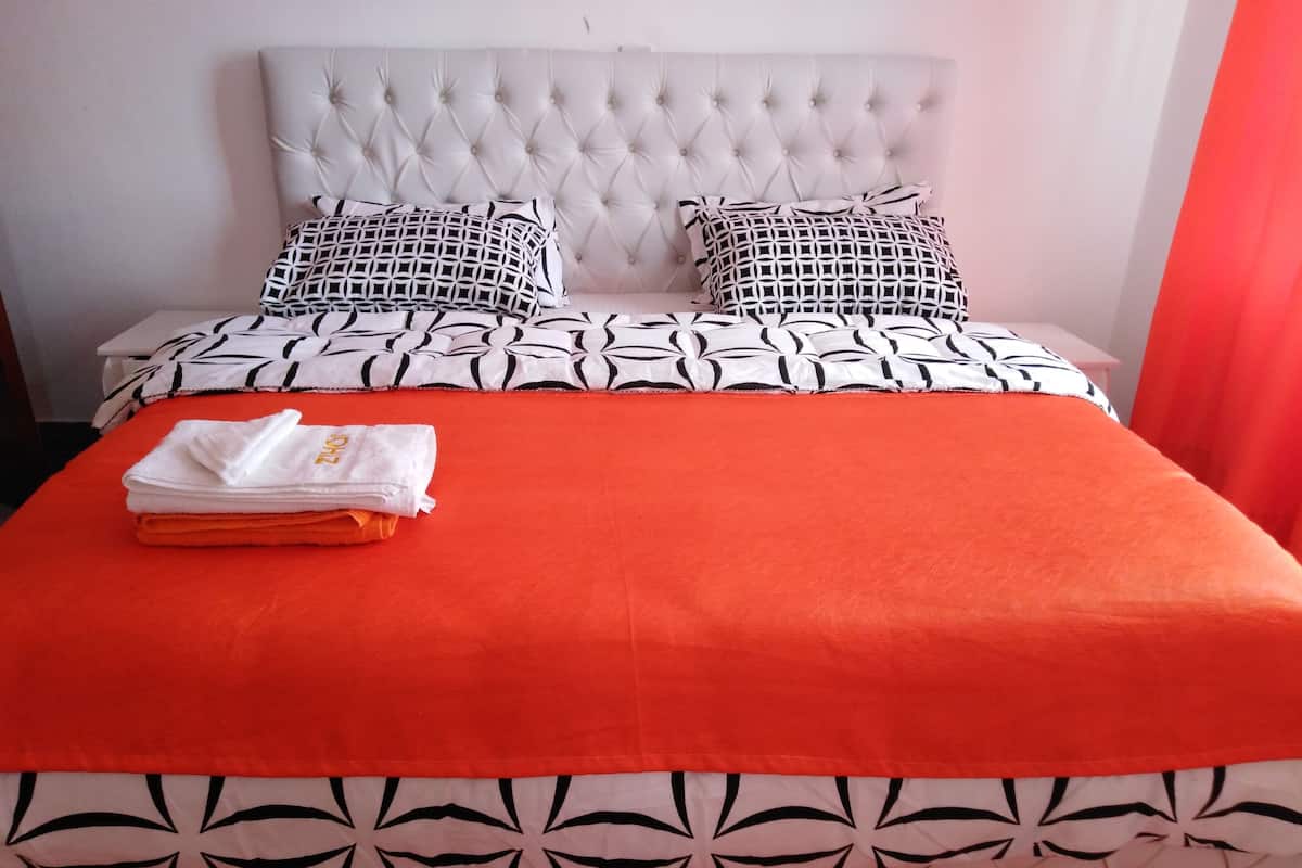 A neatly made bed with a white headboard, two patterned pillows, and an orange blanket.