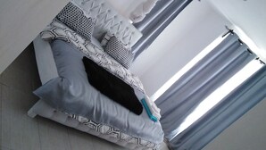 Une pièce avec un lit, une fenêtre avec des rideaux et un luminaire au plafond.