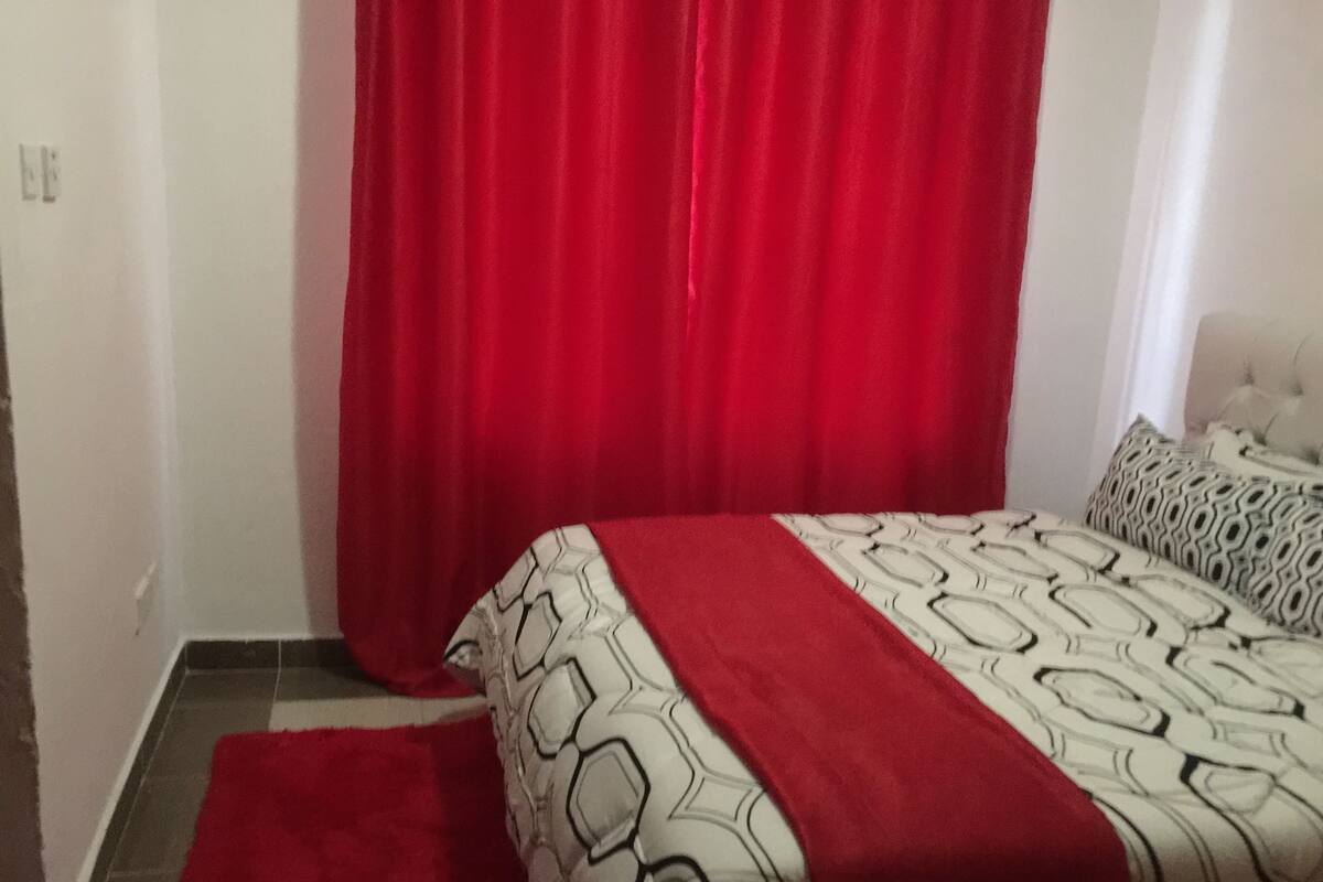 A bedroom with a bed, a red curtain, and a patterned bedspread.