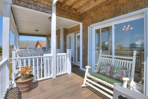 Eine überdachte Veranda mit Holzterrasse, weißen Geländern, einer Bank mit Kissen und einem Blumentopf.