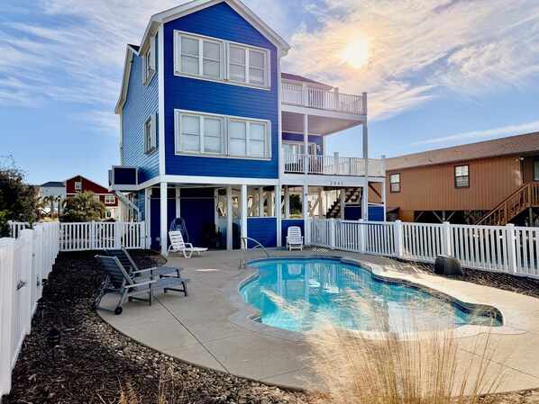 A two-story house with a swimming pool, white railings, and a clear sky.