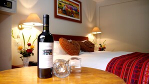 A hotel room with a bed, a bottle of wine, a glass, and a vase with flowers. - Hotel Wiracocha Inn (Machu Picchu)