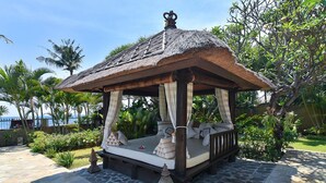 A thatched-roof gazebo with a cushioned bench, surrounded by tropical plants and a stone-paved area. - Villa Lotus - Let The Sea Set You Free (Seririt)