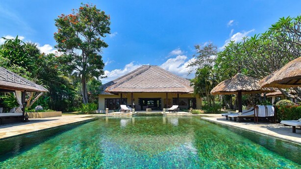 A clear pool with lounge chairs and a building with a thatched roof in the background. - Villa Lotus - Let The Sea Set You Free (Seririt)