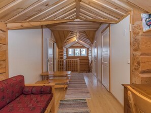 A log cabin interior with a central hallway, wooden benches, a sofa, and a window at the end. - Tainan tupa by Interhome (Sysmä)