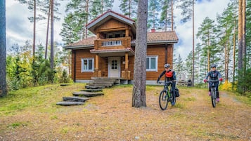 A two-story wooden cabin with a porch, surrounded by a forest.