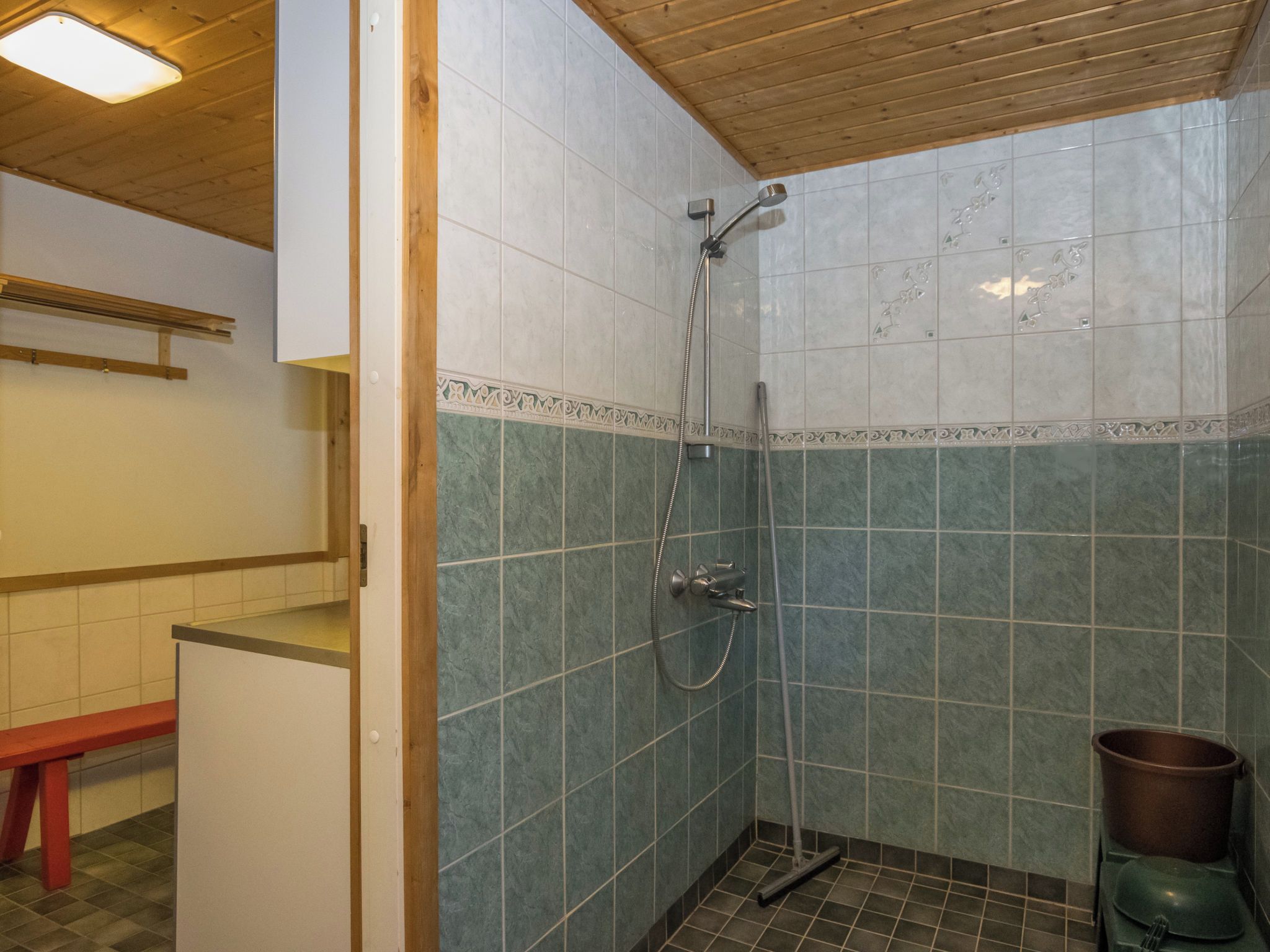 Une salle de bain avec une douche, un banc et une poubelle.
