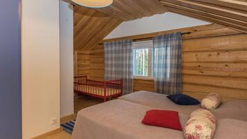 Une pièce chaleureuse avec un plafond en pente, un lit avec des oreillers, une fenêtre avec des rideaux et un fauteuil rouge.