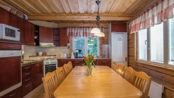 Un interior de madera con una mesa de comedor, sillas, una cocina con electrodomésticos y una ventana con persianas.