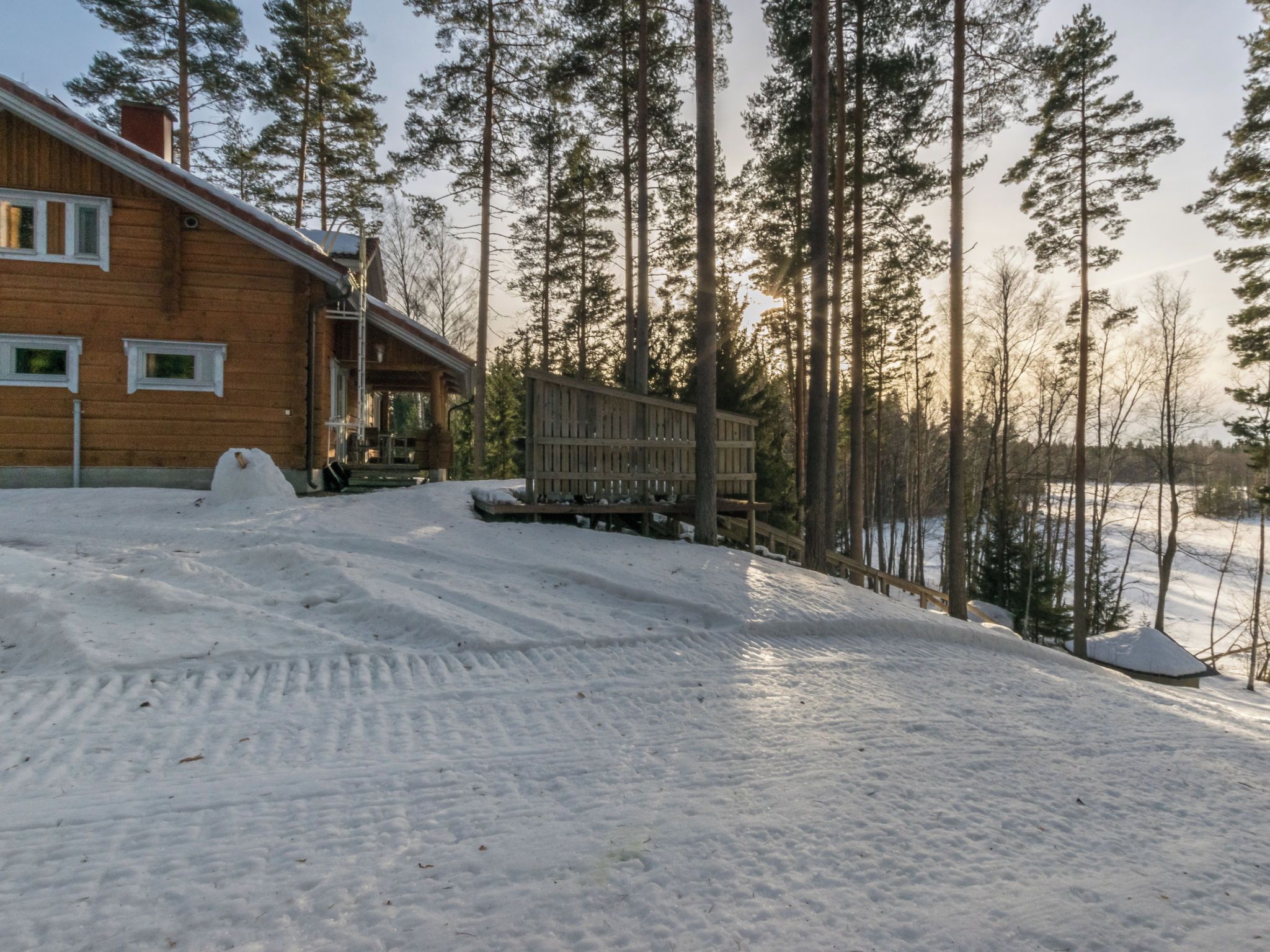 A wooden cabin with a porch, surrounded by a snowy landscape and tall pine trees.